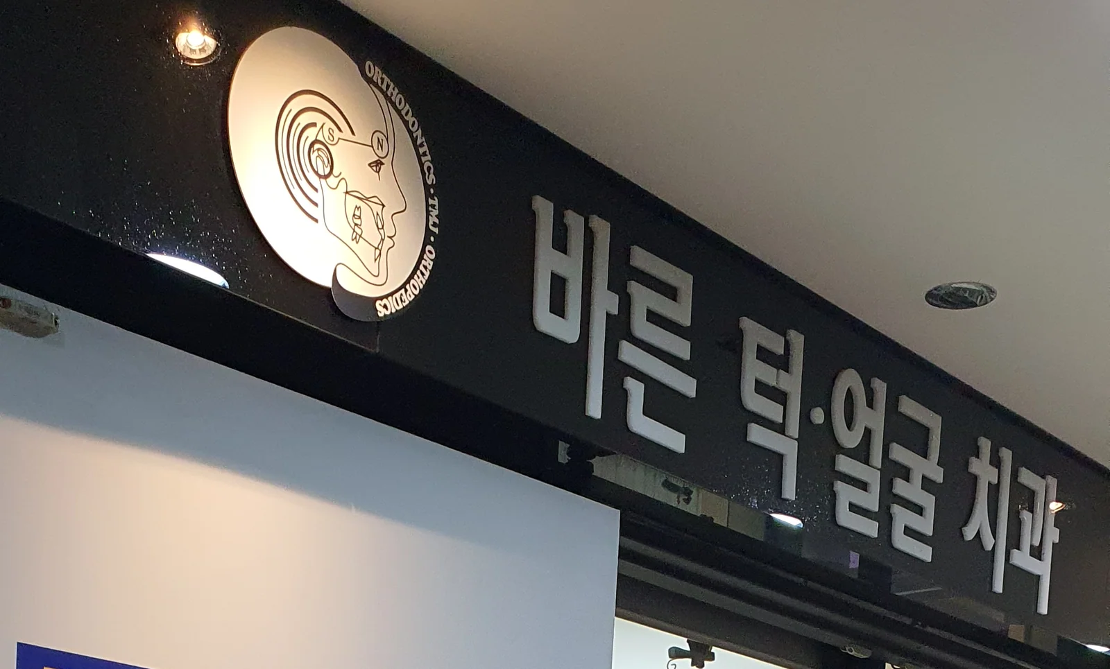 바른턱얼굴치과의원 4층 입구 사인 — 원형 엠블럼(ORTHODONTICS · TMJ · ORTHOPEDICS)과 ‘바른 턱·얼굴 치과’ 간판